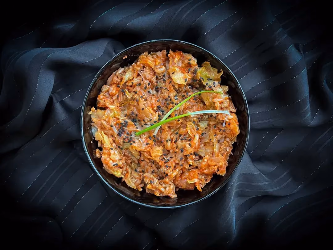 Dans un petit saladier de couleur bleu se trouve du riz basmati accompagné de boeuf haché, d'un coulis de tomate et de chou vert râpé.