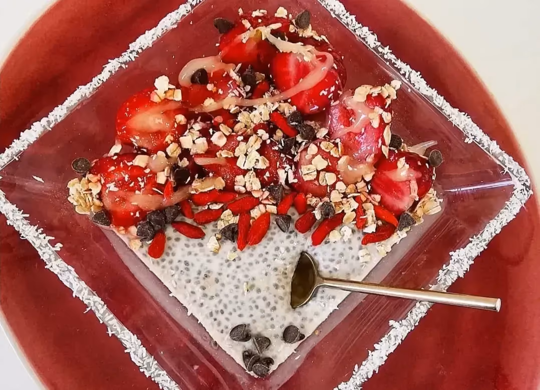 Dans un saladier carré transparent se trouvent les graines de chia ovales et grises. Quelques tomates coupées en morceaux accompagnent la préparation.