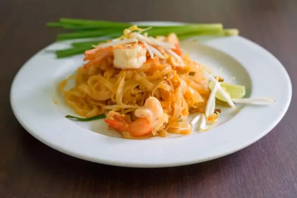 Dans une assiette creuse de couleur blanche se trouve le Pad thaï, avec les crevettes, les pâtes de konjac et des germes de soja.