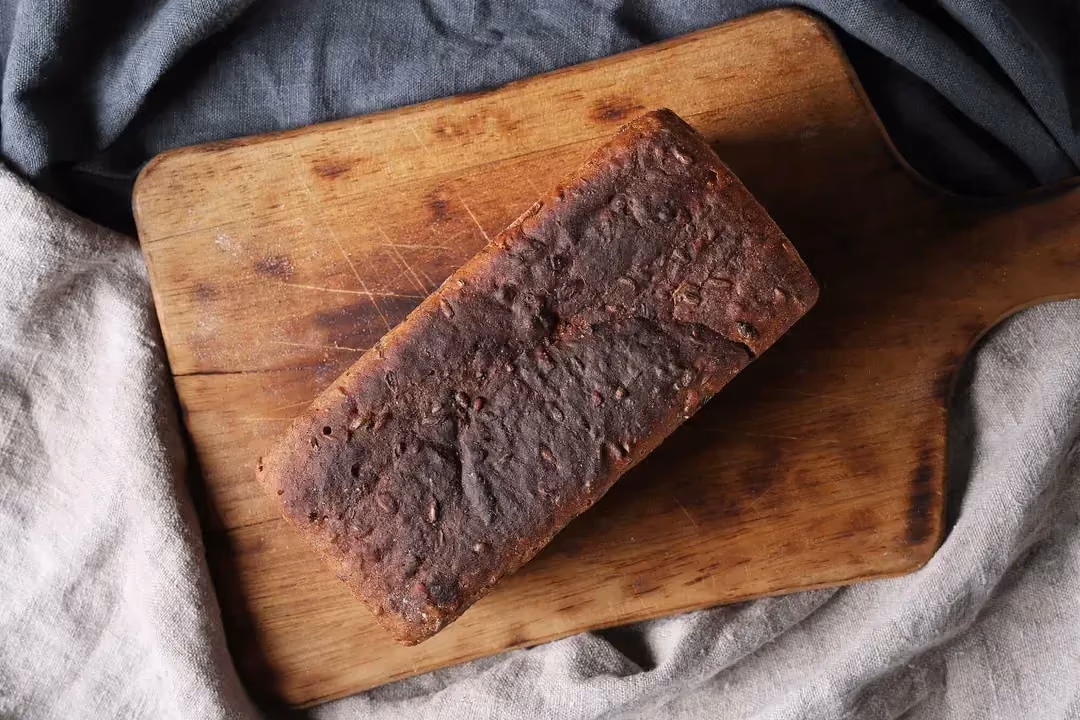 Le pain au son d'avoine de couleur brune bien grillé est posé sur une planche à découper avec des torchons gris autour.