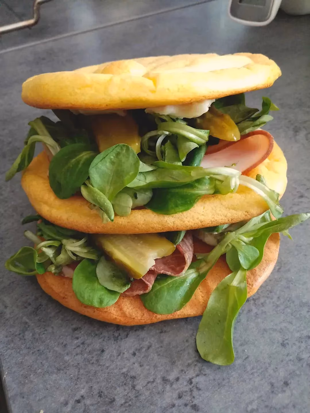 Trois pains nuages servent à l'élaboration d'un sandwich appétissant, comprenant de la salade, du jambon de Parme et des cornichons coupés en deux.