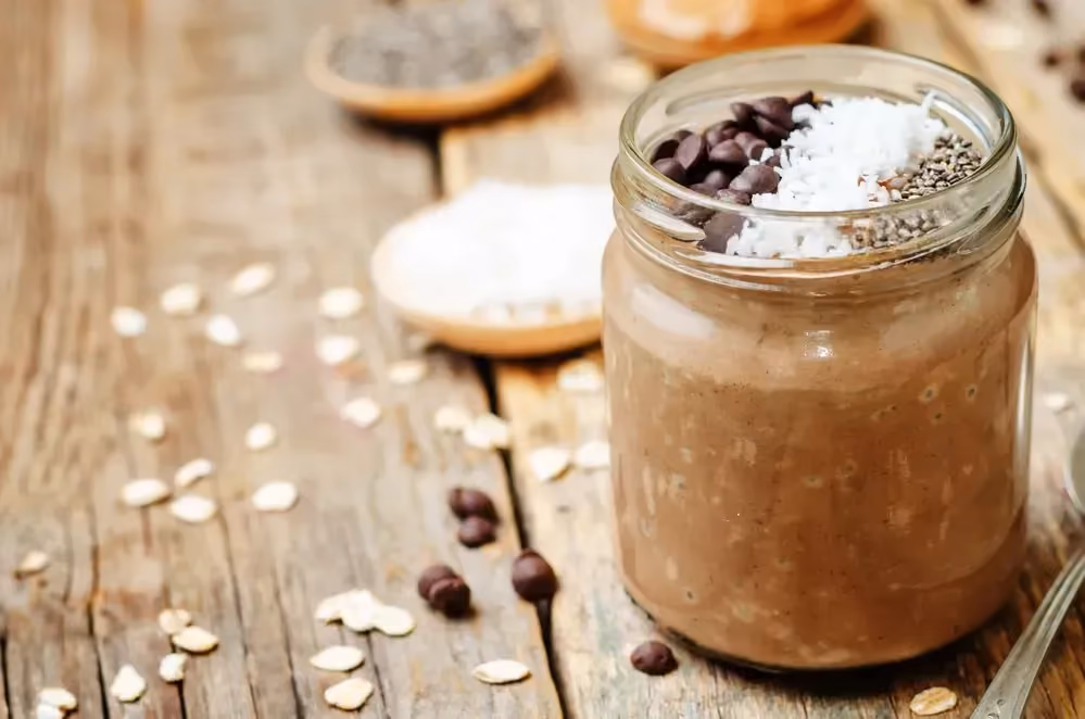 Dans un bocal à viser se trouve le mocha overnight oats. Quelques pépites de chocolat sont à côté.