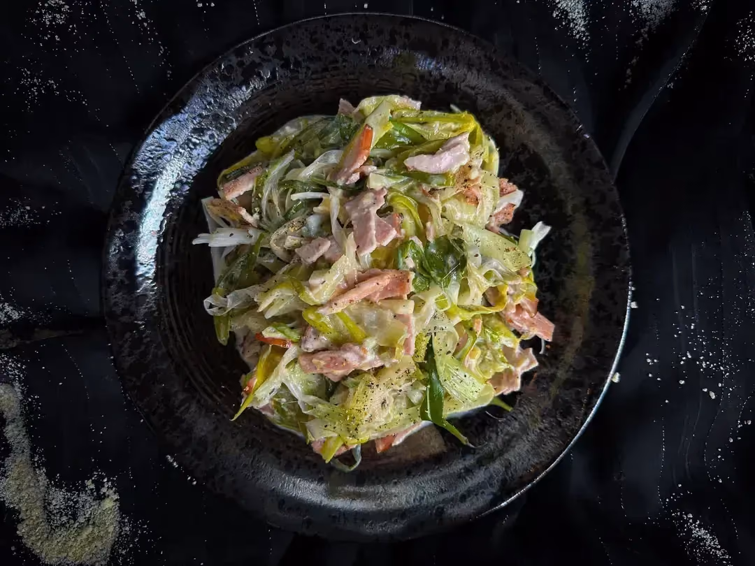 Leek spaghetti with goat cheese and bacon are served in a blue earthenware dish.