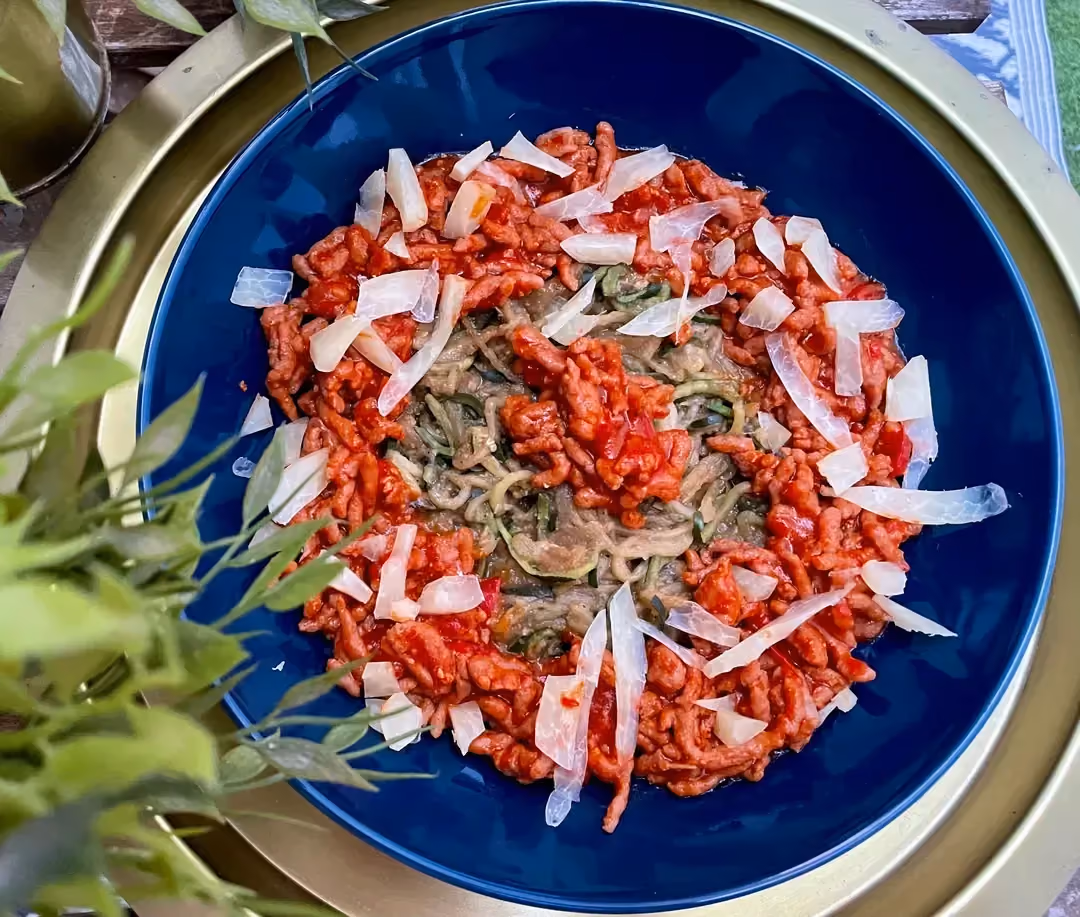 In a blue bowl, zucchini noodles are served with ground beef mixed with tomato sauce.