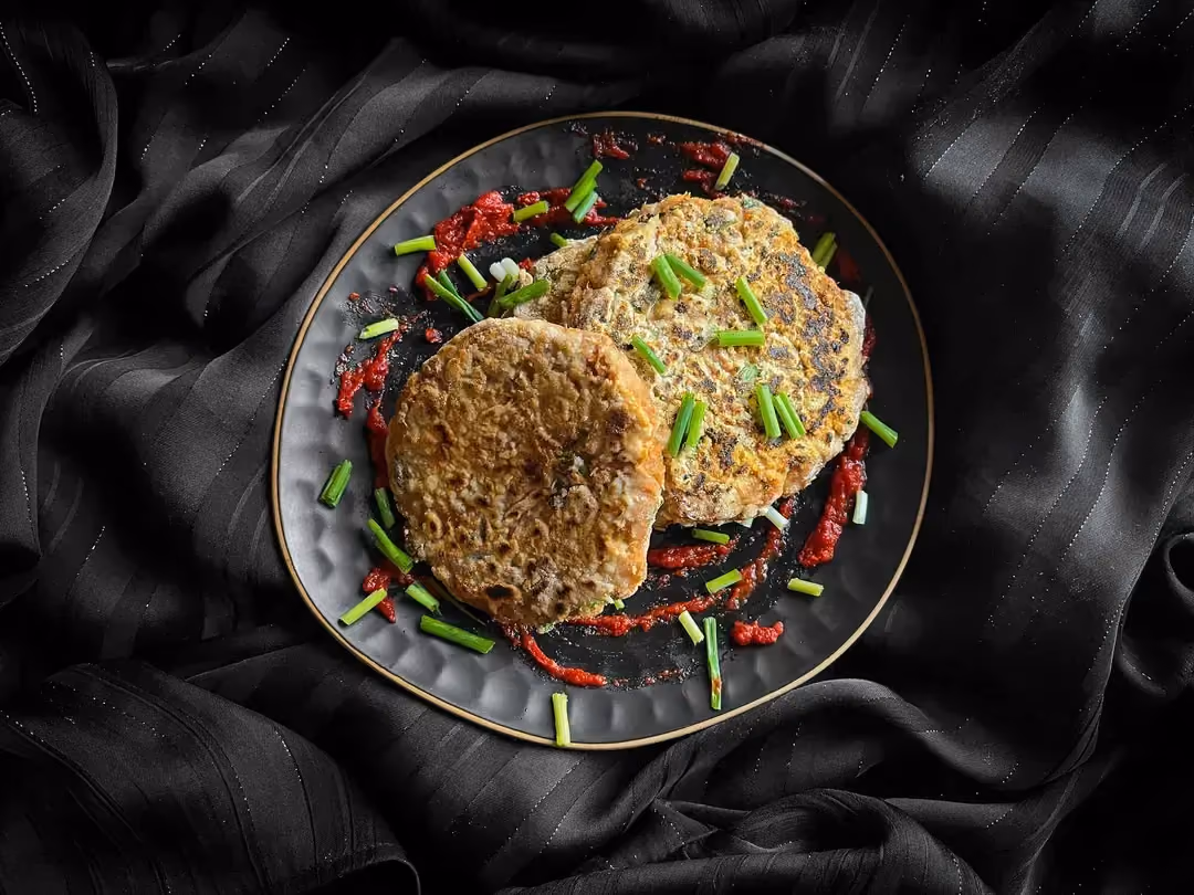 Trois steaks de thon façon burger sont disposés dans un petit saladier alvéolé de couleur bleue. De la ciboulette fraîche émincée accompagne le plat.