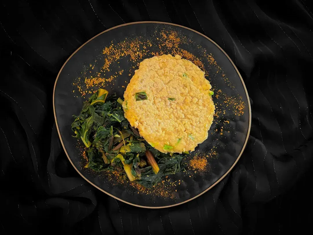 At the bottom of a beautiful blue salad bowl is a round salmon steak. It is served with pan-fried Swiss chard.
