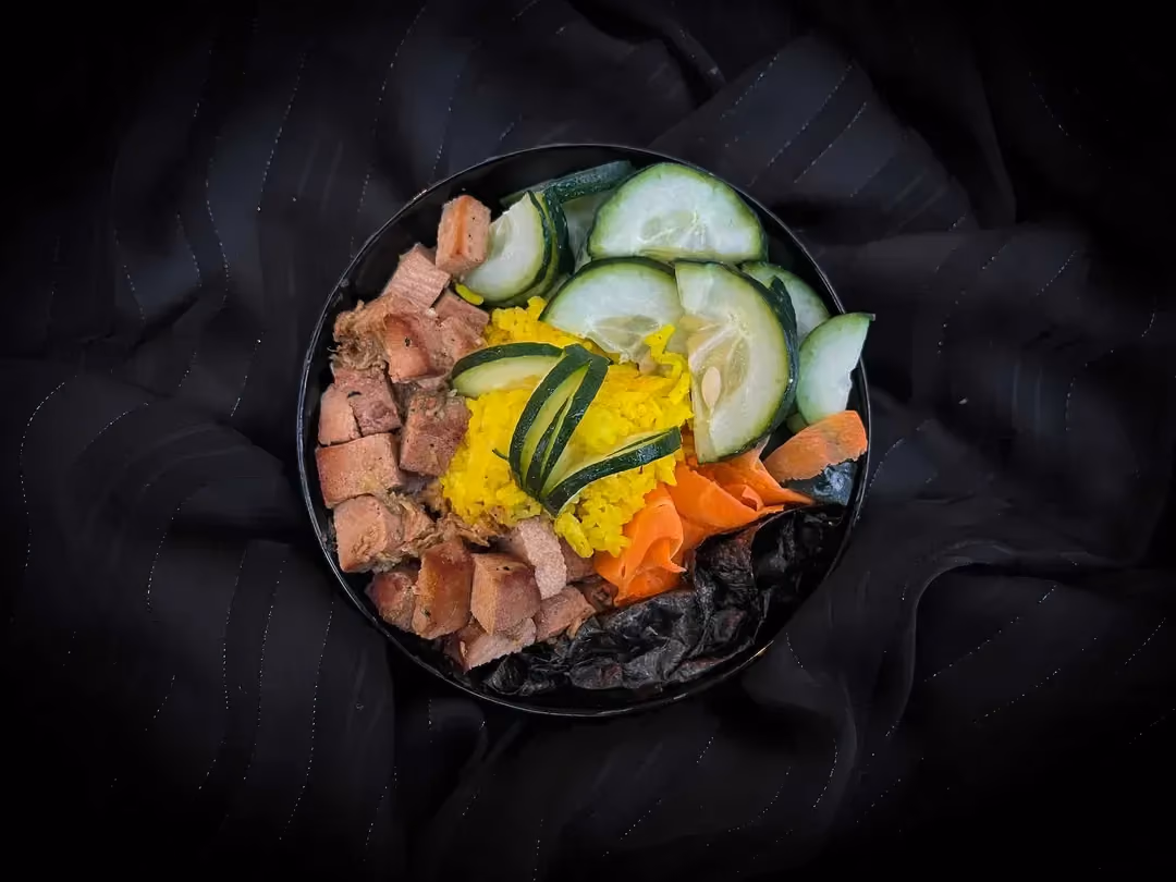 In a bowl, on a bed of rice, there is tofu cut into small cubes, with cucumber sliced into thin strips. Saint Moret ties it all together.