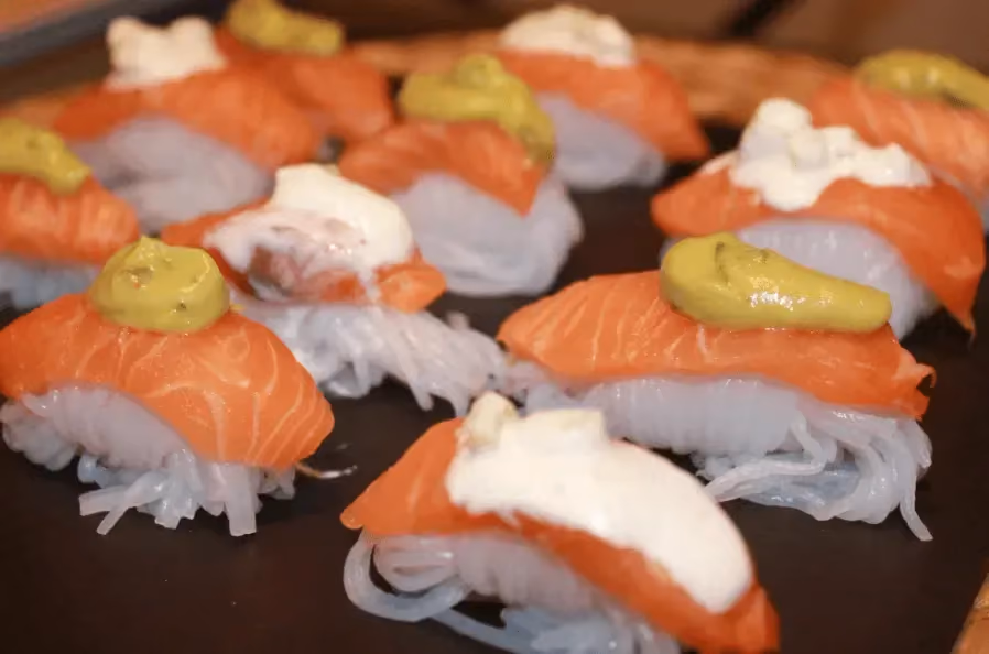 Une douzaine de sushis de saumon sont disposés sur un plat peu profond de couleur noir.
