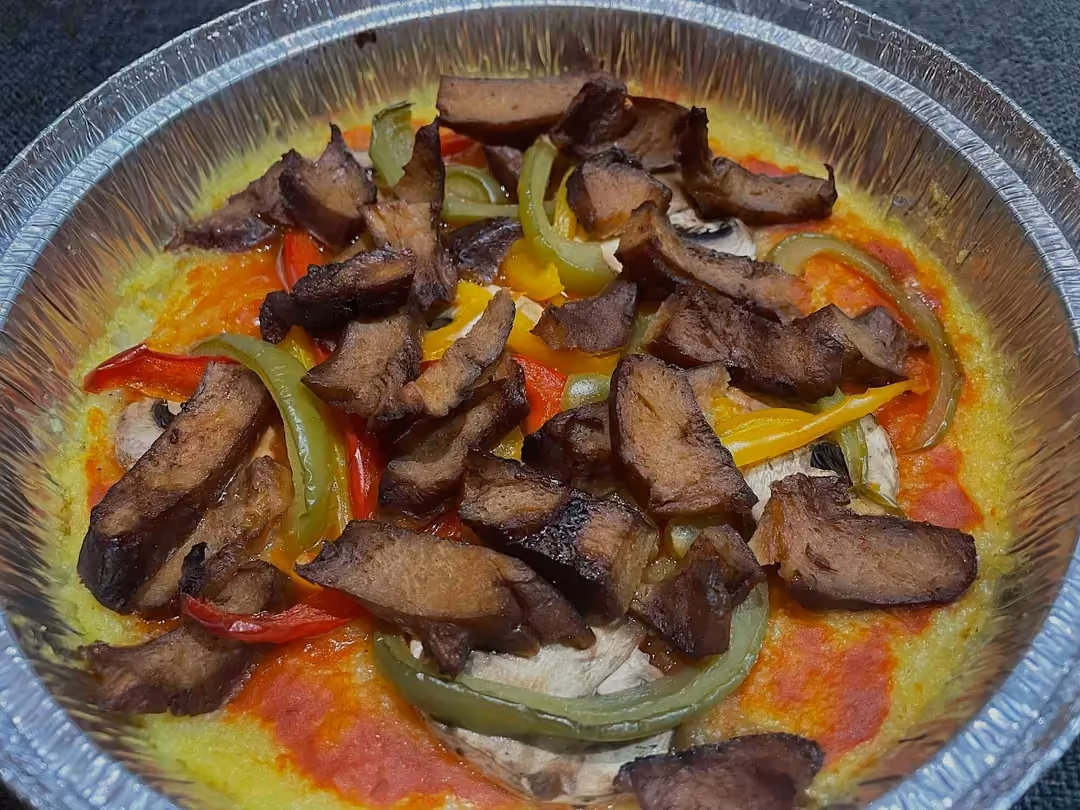 Dans un plat de cuisson rond en alu, la polenta est recouverte de sauce tomate. Le seitan et les poivrons donnent une touche de couleur à l'ensemble.
