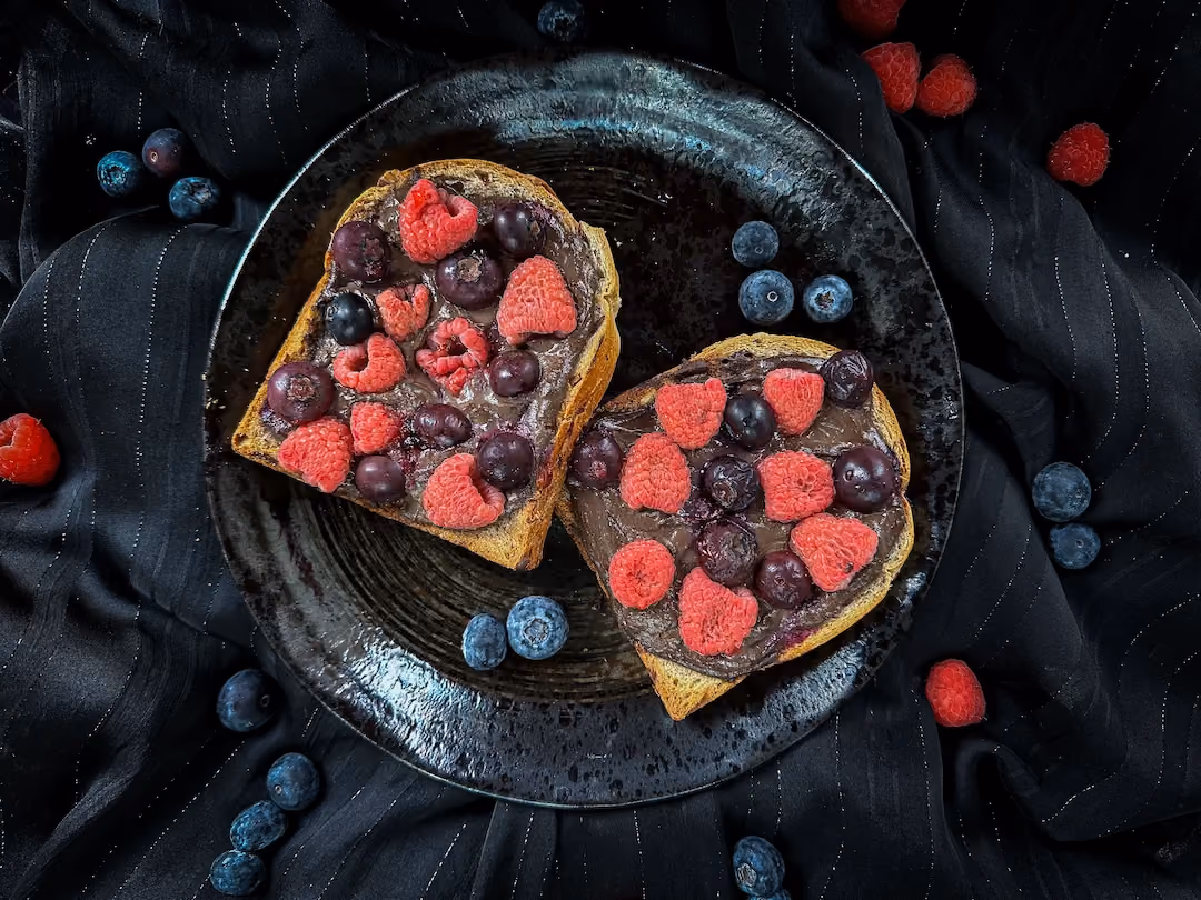 Sur une assiette de couleur noire se trouve deux grosses et belles tranches de pain au four. Les fruits rouges apportent une belle touche de couleur.