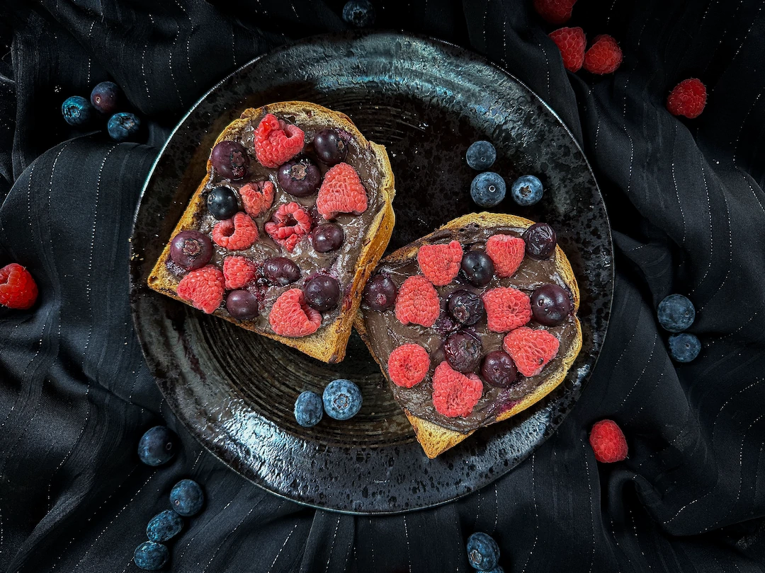 On a black plate, there are two large, beautiful slices of oven-toasted bread. The red berries add a lovely touch of color.
