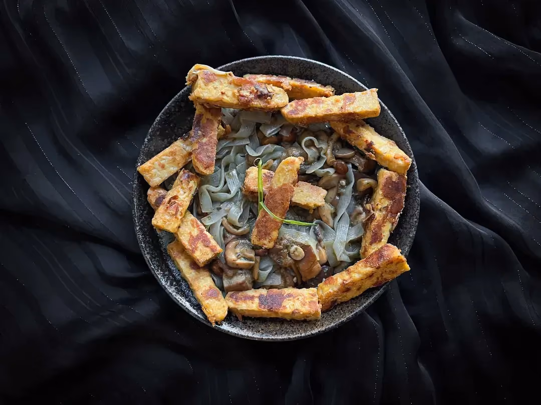 La recette de tempeh mariné au sirop d'érable et cacahuiètes accompagné de champignons et konjac est présentée dans un petit saladier de couleur bleu.