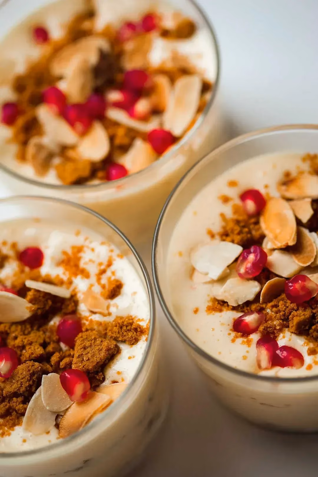 Ce tiramisu est présenté dans trois verrines et il est décoré de spéculoos émiettés, de grenades et d'amandes effilées.