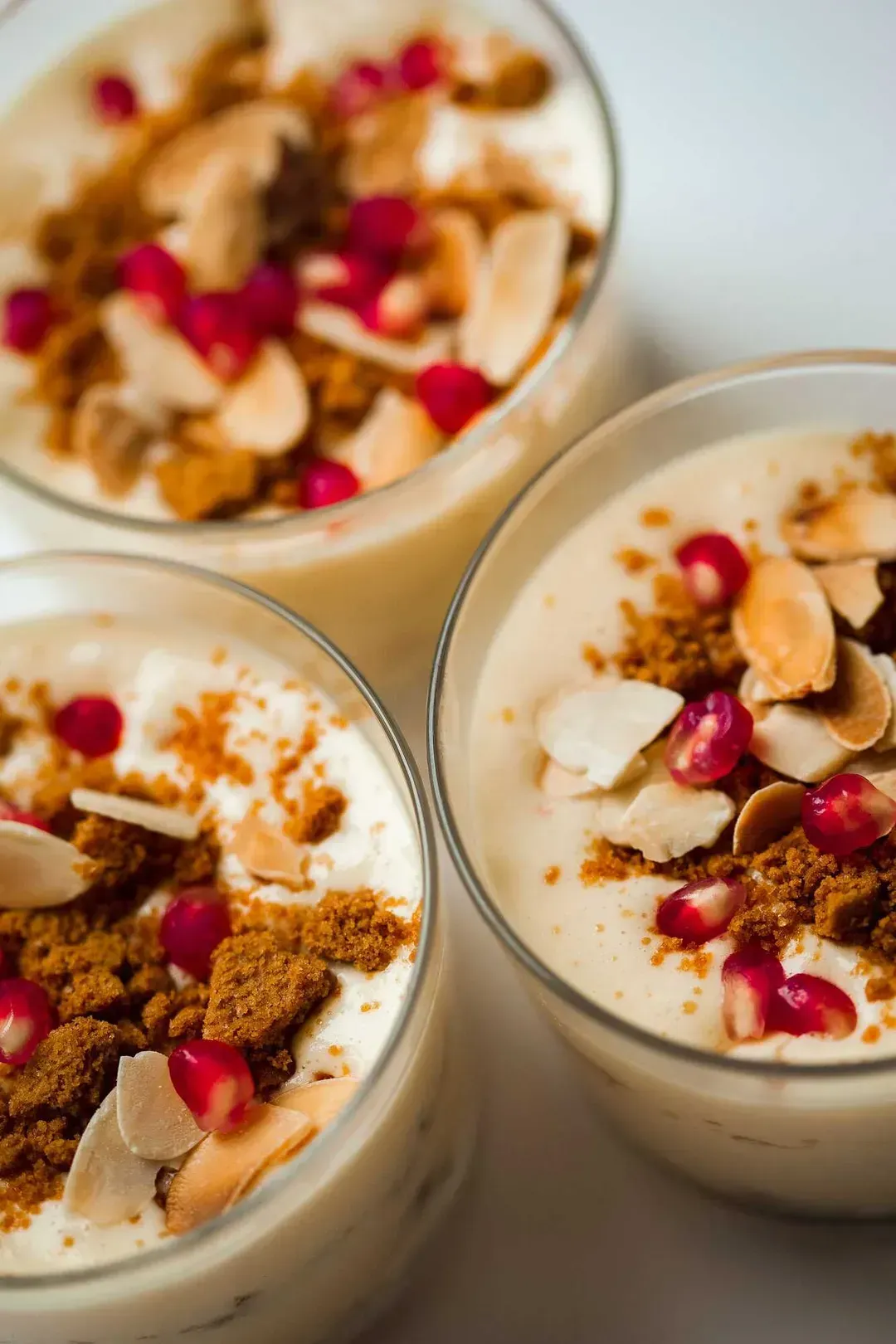 This tiramisu is served in three verrines and topped with crumbled speculoos cookies, pomegranate seeds, and sliced almonds.
