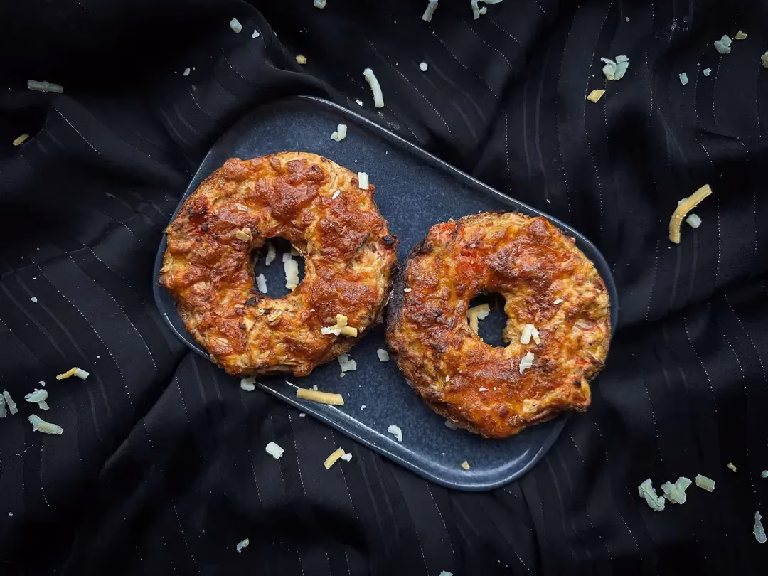 Le bagel au thon, fromage frais et fromage râpé coupé en deux partie est présenté sur un plat rectangulaire peu profond de couleur bleu.