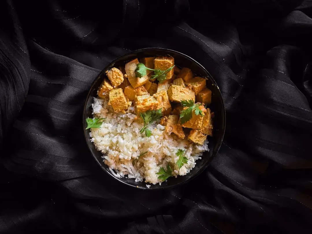 Dans un joli bol de couleur bleu alvéolé se trouve le tofu coupé en gros cubes et le riz de chou fleur.