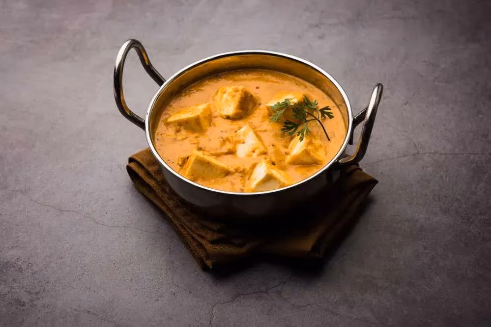 Posée sur un torchon marron plié en plusieurs épaisseurs, une marmite en aluminium contient de gros morceaux de tofu colorés par la sauce tomate.