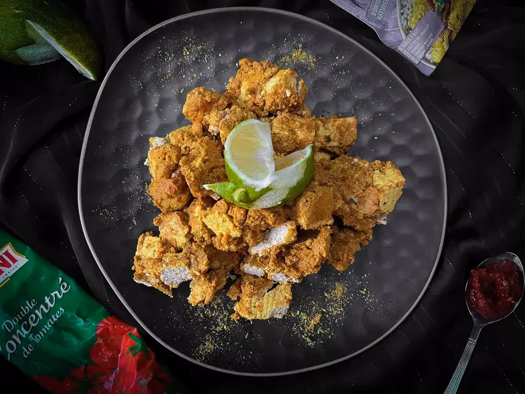 Dans un bol se trouve le tofu aux épices tikka qui est mélangé à de la sauce tomates. Au dessus se trouve de fines tranches de citron jaune.