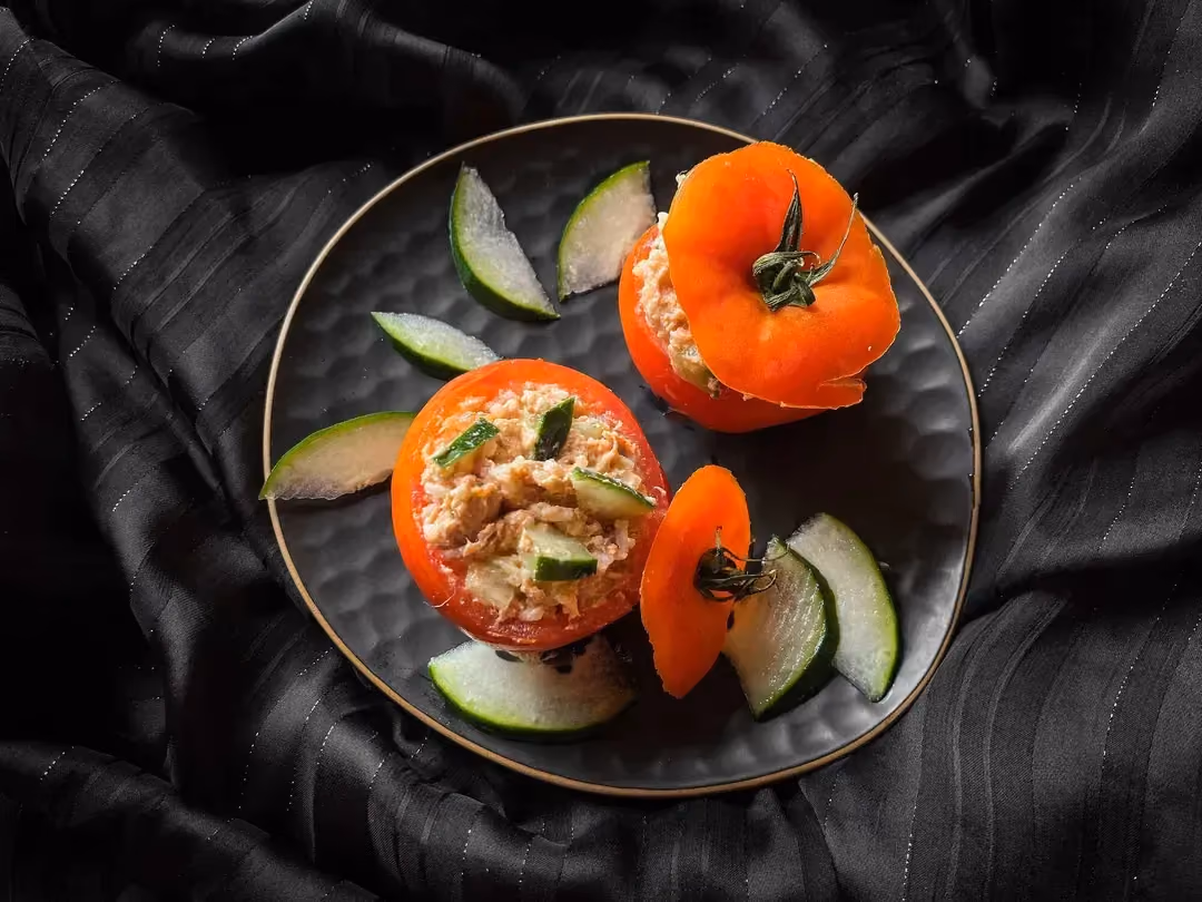 In a small salad bowl, there are two large tomatoes stuffed with tuna, basmati rice, and tomato flesh.