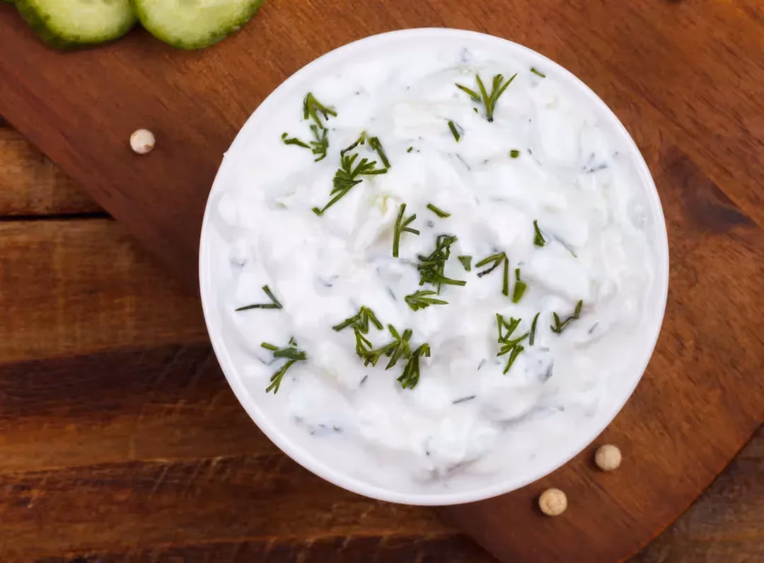 Le Tzatziki est présenté dans une petite soupière de couleur blanche. A côté du plat se trouve des tranches de concombres.