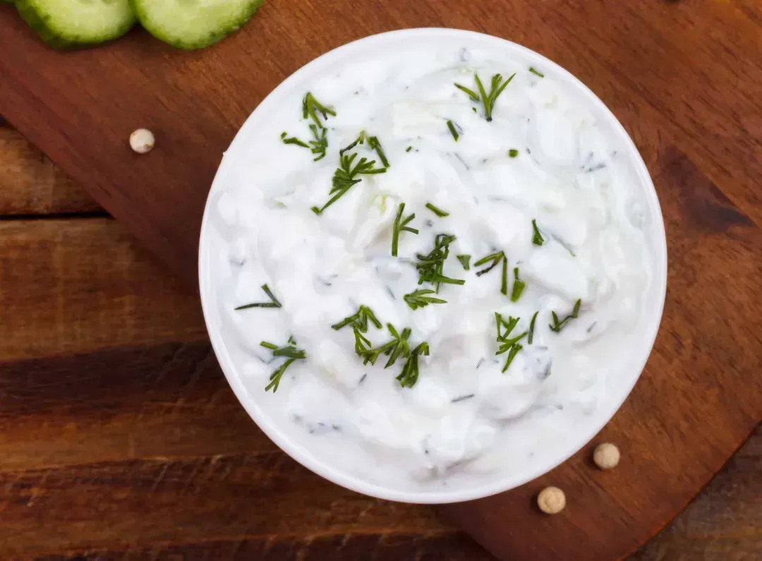 The Tzatziki is presented in a small white soup bowl. Next to the dish are slices of cucumber.