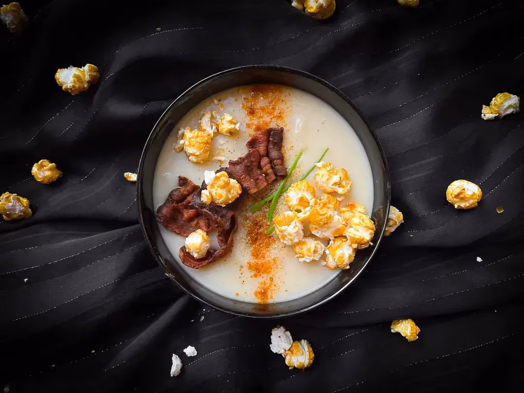 In a bowl is the cauliflower velouté, topped with a few bacon chips and some popcorn.