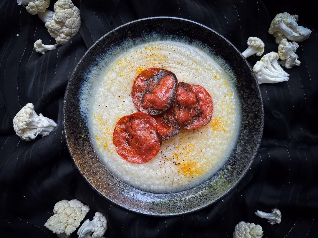 In a large bowl, there is a smaller bowl containing cauliflower velouté with chorizo.