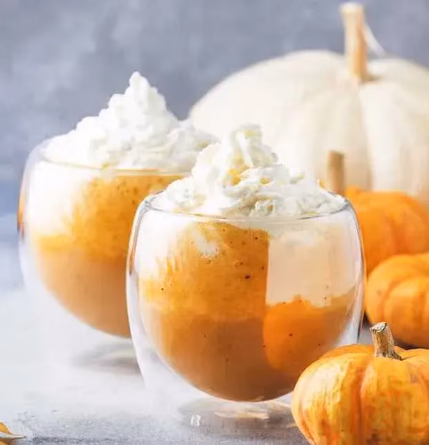 Deux grosses verrines reçoivent la préparation à base de citrouille. De la crème Chantilly sert de topping. Trois petites citrouilles sont à côté.