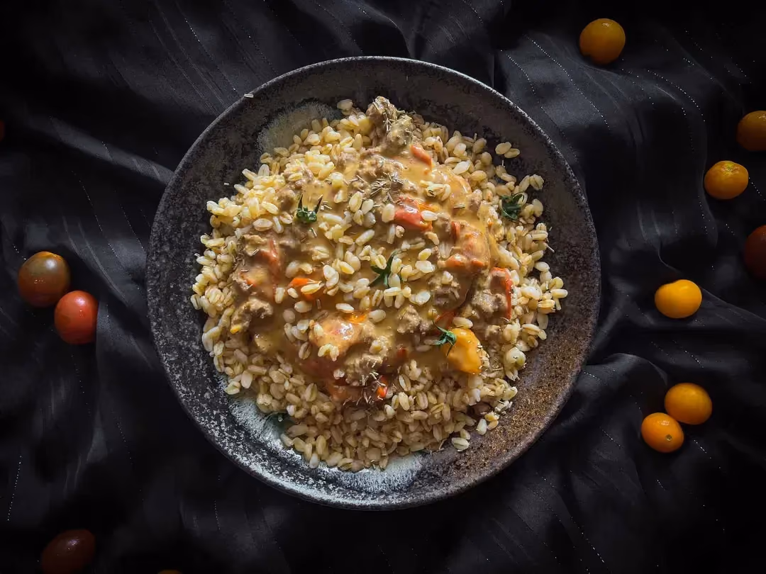 In a small bowl is the ground beef and wheat recipe with cheddar sauce. A few cherry tomatoes are next to the dish.