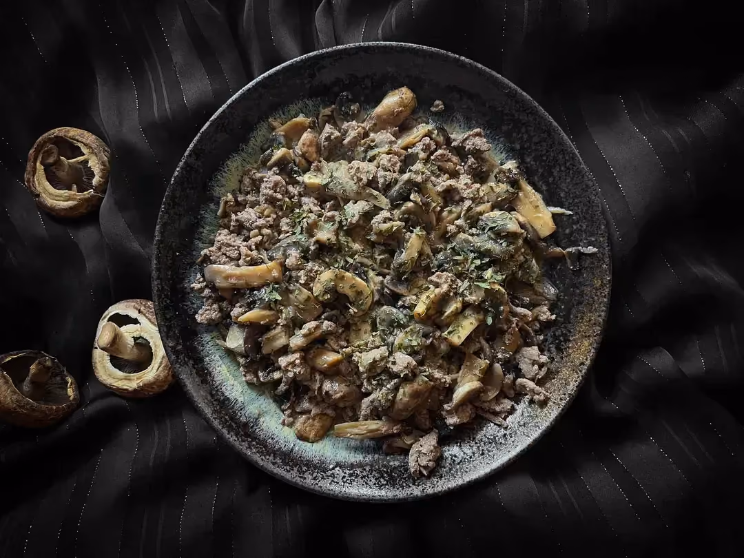 Dans un petit saladier de couleur bleu se trouve la recette de viande haché et sauce aux champignons de Paris. Trois champignons sont à côté du plat.