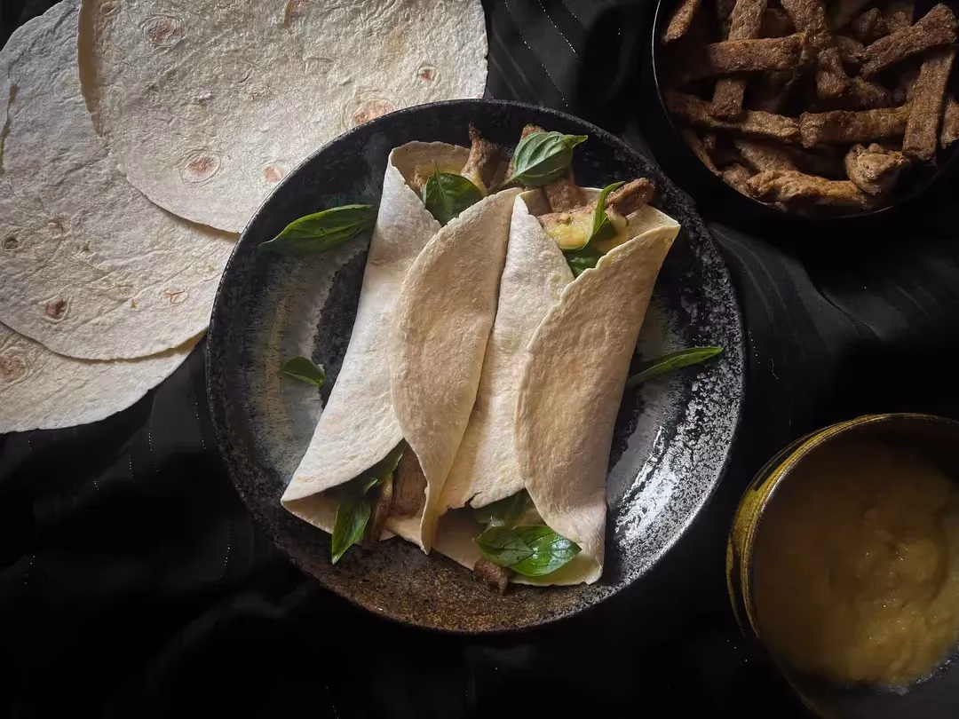Two wraps with soy strips, basil and pumpkin purée are presented in a small bowl. The soy strips are in a bowl.