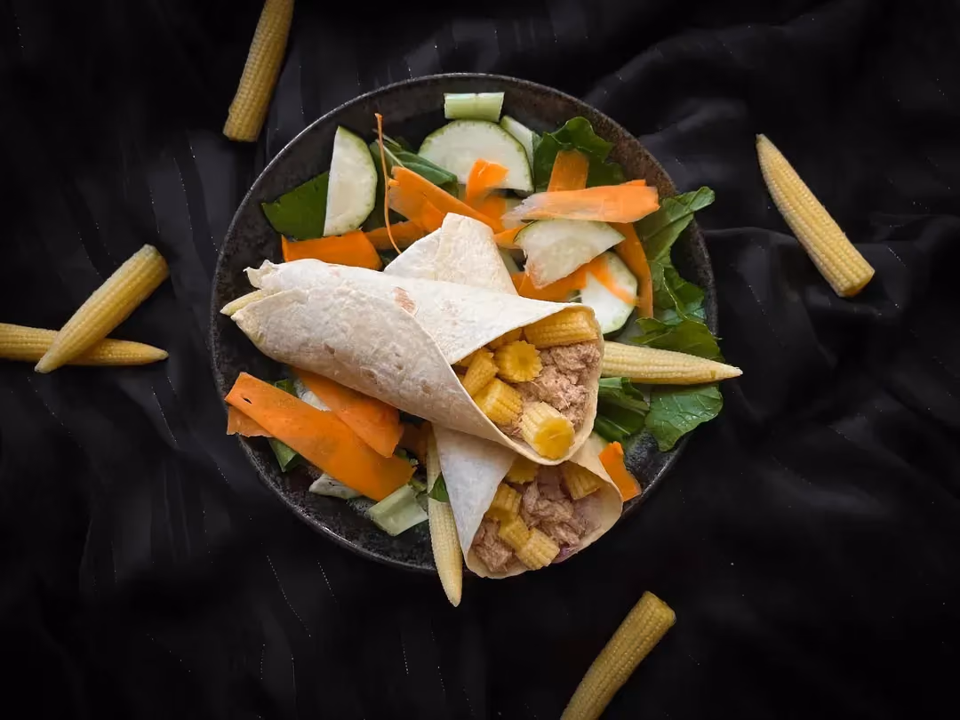 Two tuna, corn, and sour cream wraps are presented in a small bowl. Five small pieces of corn are placed next to the dish.