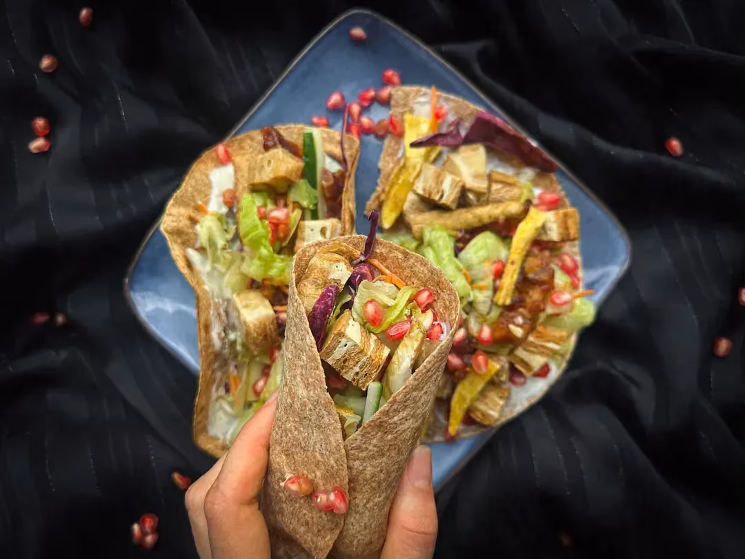 Posés sur un plat noir, se trouve cinq wraps à base de patate douce, grenades, dattes et soja. Autour se trouve un demi citron vert et le l'ail.
