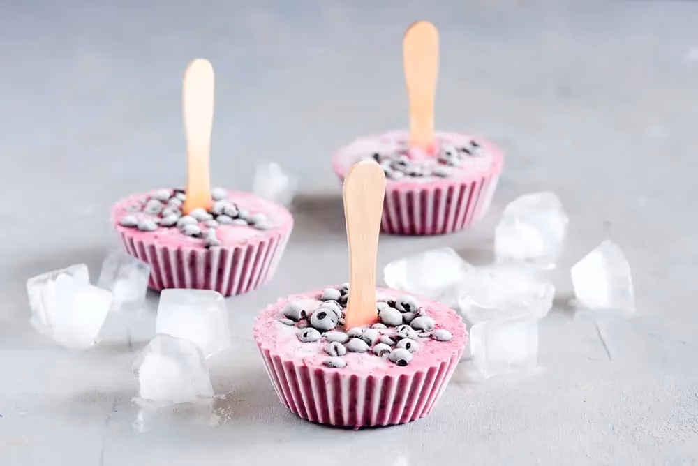 Trois yaourts glacés sont présentés dans des petits moules à muffins. De gros glaçons sont posés tout autour.