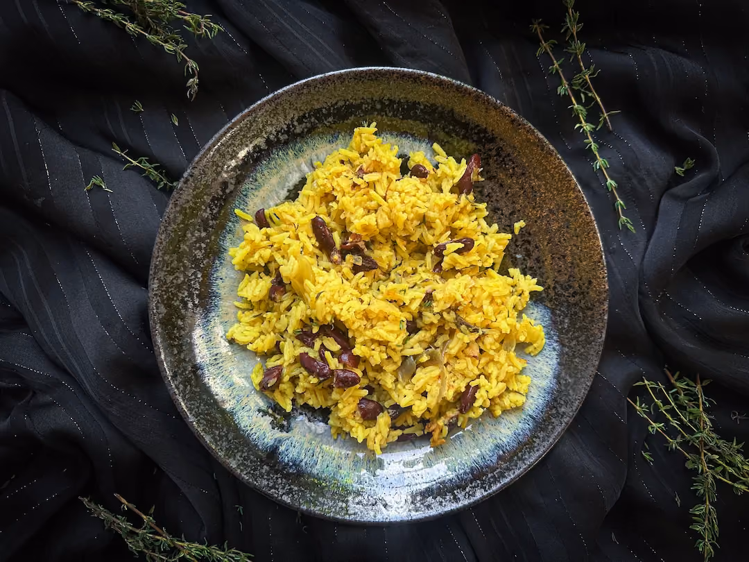 The zembrocal is served in a black earthenware dish. The beans and rice have taken on the color of saffron.