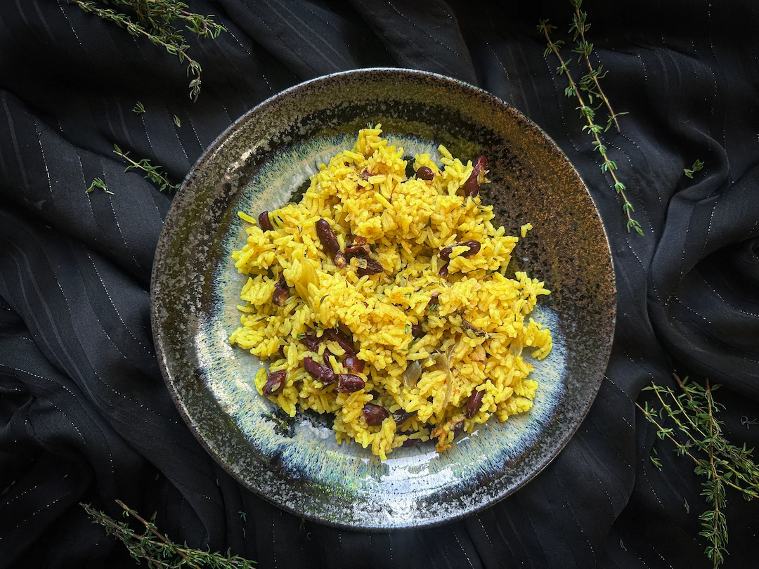 The zembrocal is served in a black earthenware dish. The beans and rice have taken on the color of saffron.