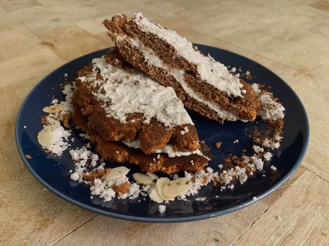 Deux pancakes sont présentés sur une assiette de couleur foncé, ils sont recouverts de chocolat et de noix de coco râpée.