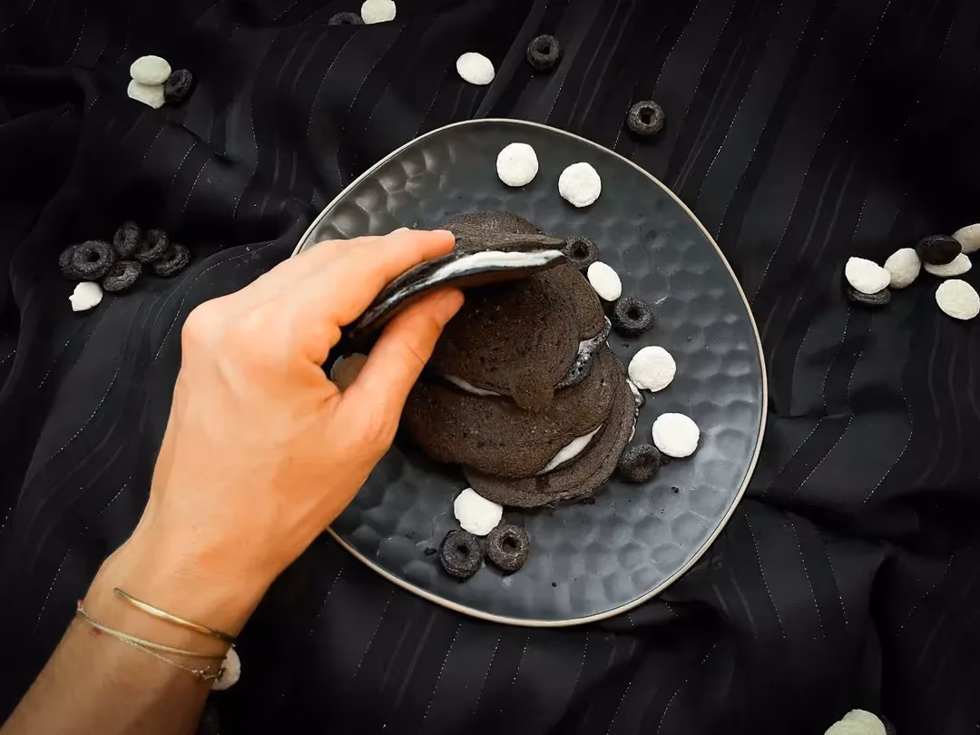 Dans la main gauche de Maëlle se trouve un pancake au chocolat en poudre non sucré, au dessus d'un plat de couleur bleu alvéolé.
