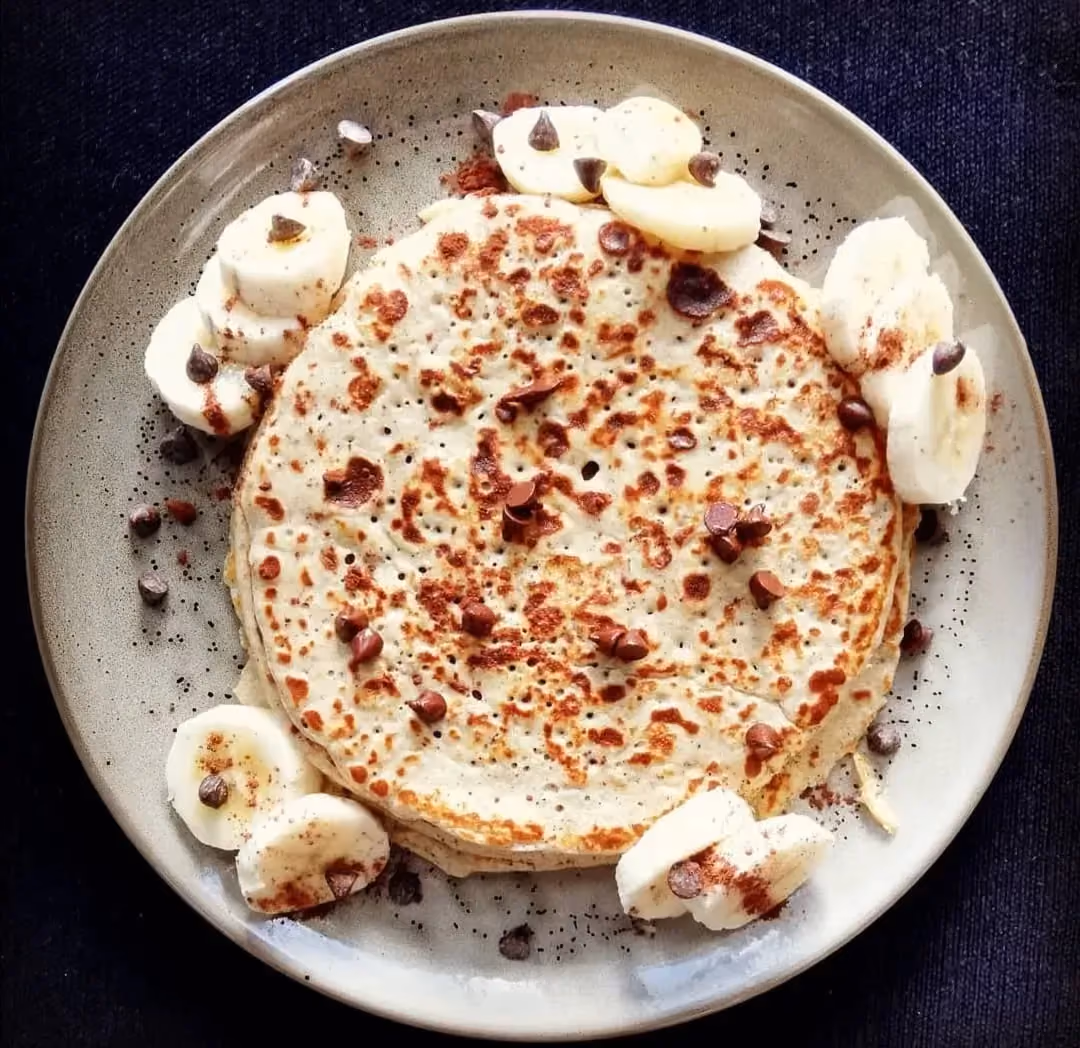 In a deep beige stoneware plate, the pancakes are stacked on top of each other. Banana slices are arranged around the plate.