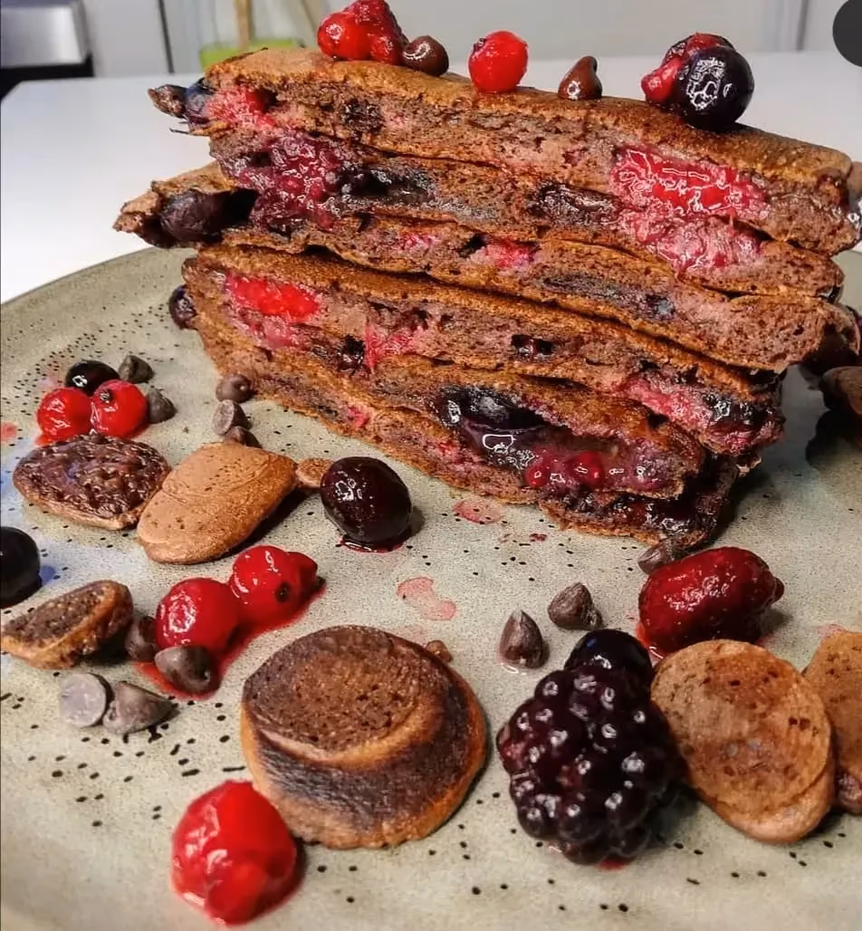Sur un large plat en grès, les Pancakes fourrés sont empilés les uns sur les autres. A côté il y a quelques fruits rouges et des petits snacks sucrés.