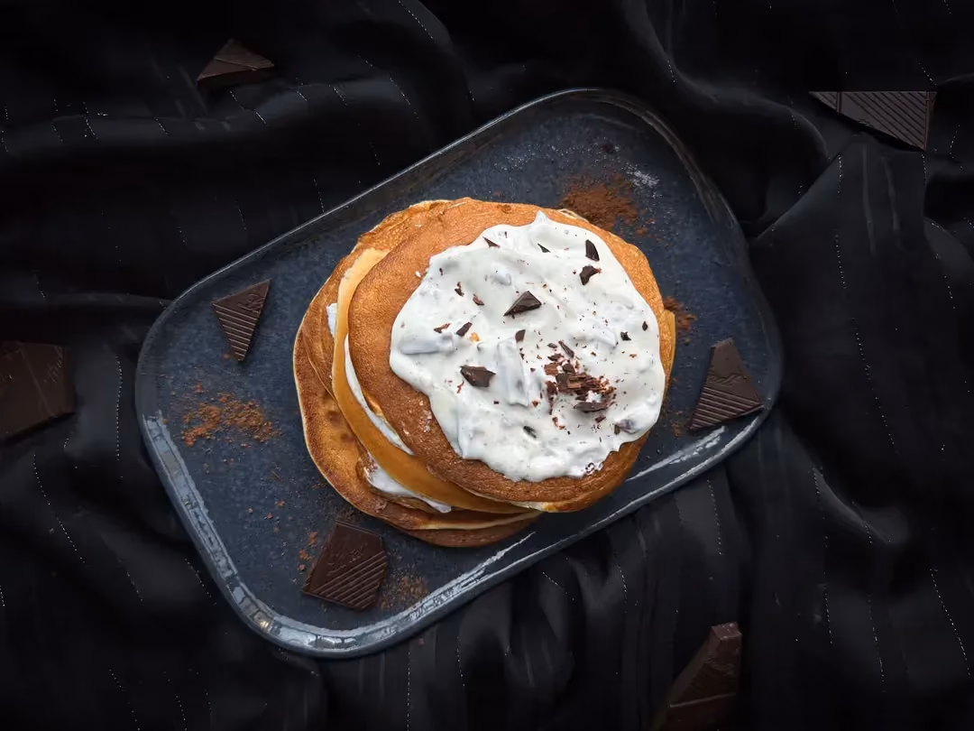 Les pancakes avec leur topping composé de skyr et de chocolat sont empilés sur un plat peu profond de couleur bleu.