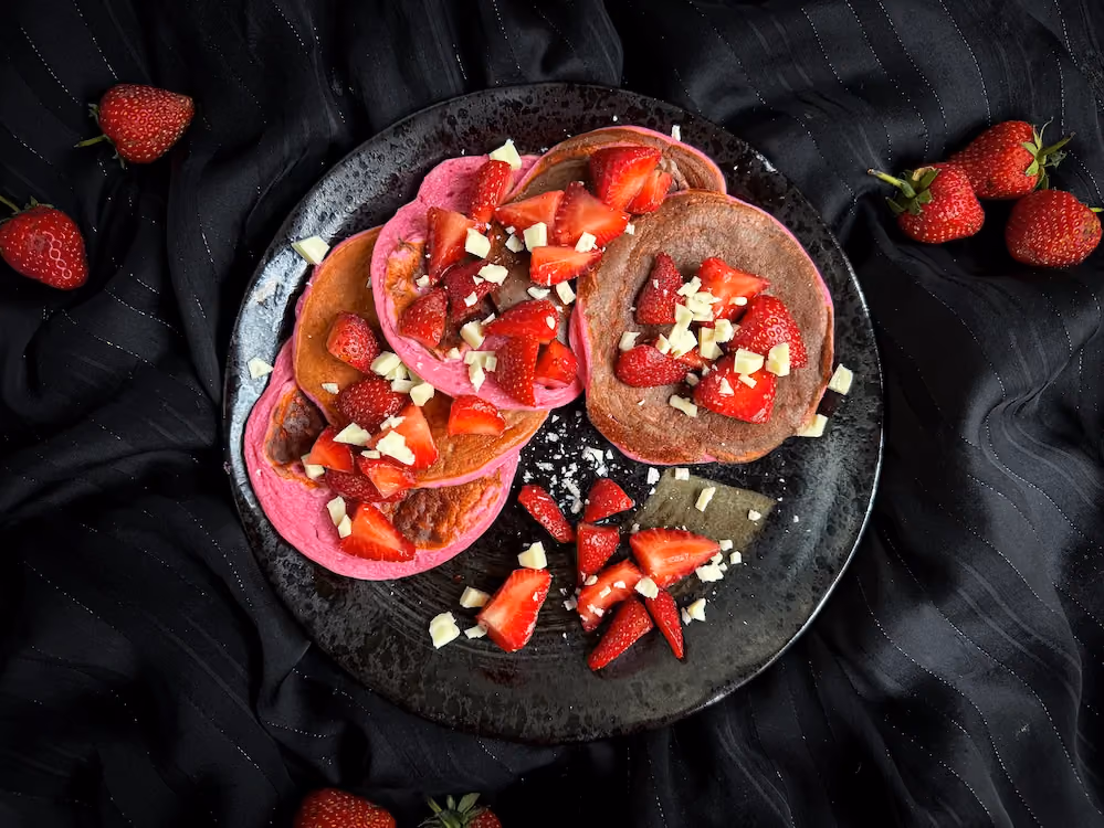 Les pancakes sont empilés au milieux d'une jolie petite assiette noire, les fraises et le chocolat blanc servent de topping.