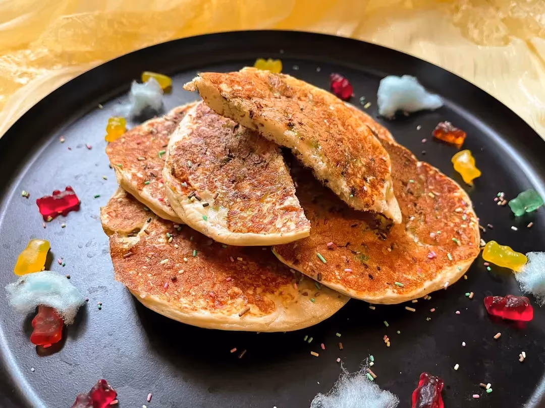 Sur une poêle non-adhésive se trouve quelques pancakes ricotta et pistache. Des petites douceurs sucrées de la marque Haribo sont disposées autour.