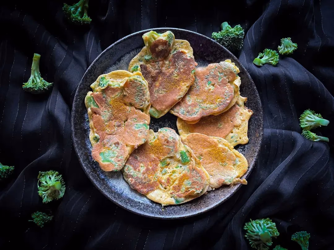 Savory broccoli pancakes are presented in a small blue bowl. A few broccoli florets are placed around the bowl.