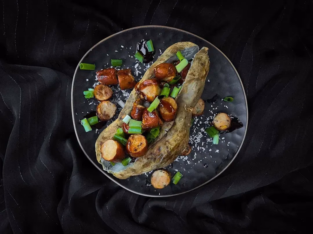 In a large blue bowl, a sweet potato cut in half is topped with sliced poultry sausage.