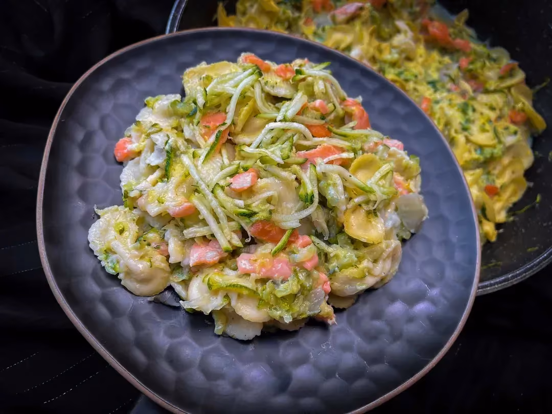 Dans un jolie plat de couleur bleu se trouve du saumon fumé, des pâtes à la sauce Béchamel et des courgettes râpées.