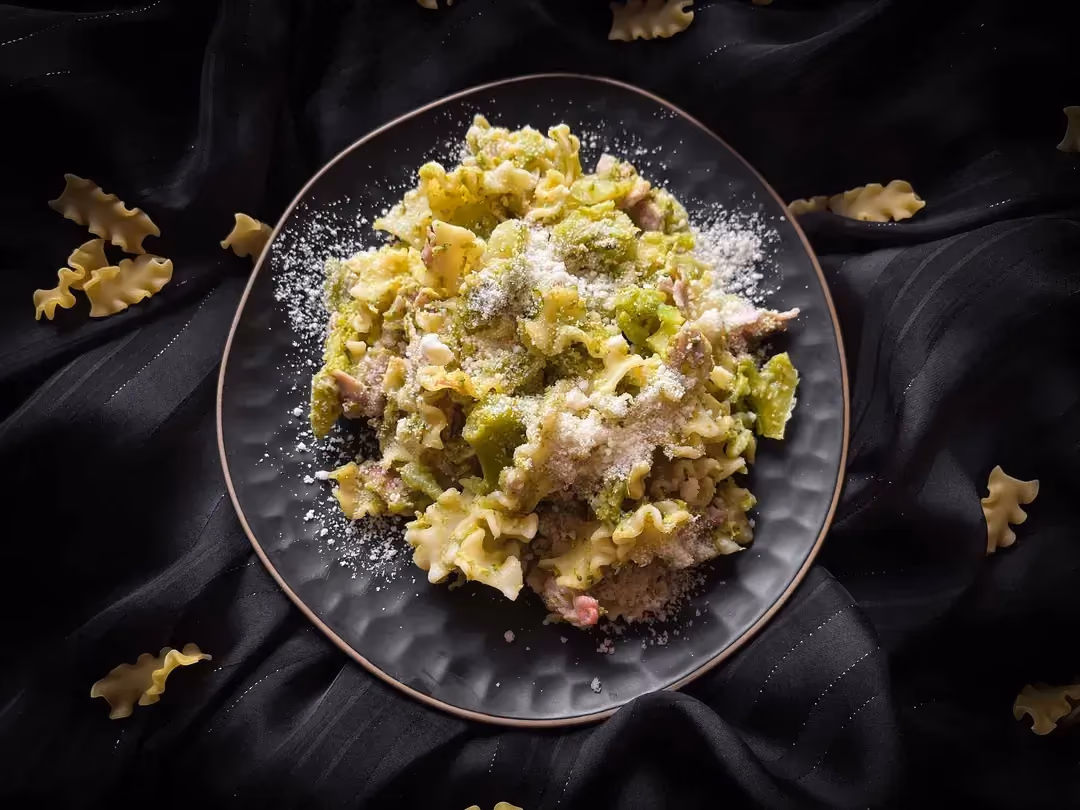 In a small blue textured bowl, there is broccoli pasta with bacon. Finely grated Parmesan covers the entire dish.