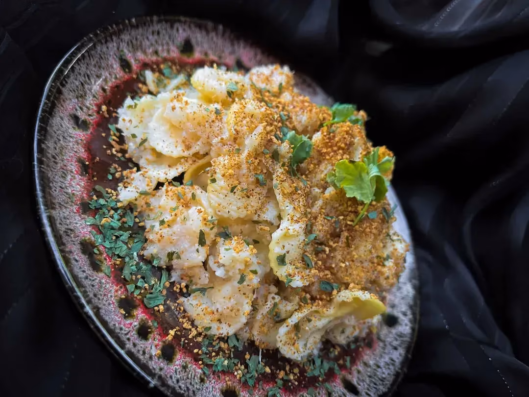 Sur une belle assiette plate se trouve les pâtes au chou-fleur et le poulet coupé en petits cubes. Le tout est saupoudré de panure et de parmesan.