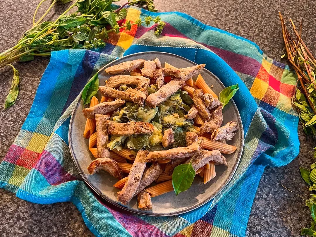 Un saladier posé sur un torchon multicolore, reçoit les pâtes de lentilles à la crème de courgettes avec du basilic.