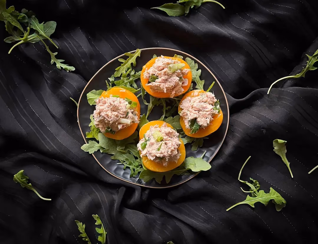 A small perforated bowl holds four beautiful peach halves topped with tuna mixed with Saint Moret. Everything sits on a bed of chives.
